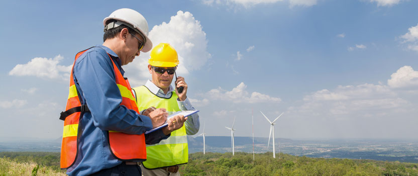 Male Engineer and Architect working Together with Hand-Held Transceiver Radio and Clipboard at Wind Turbine Power Generator Field as infrastructure construction Project Development Teamwork